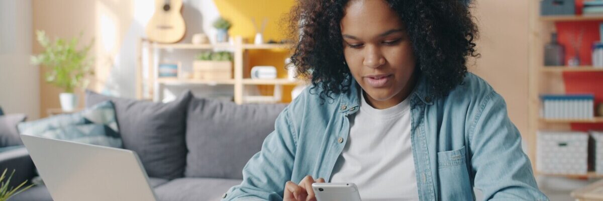 Young woman using phone at desk with laptop.