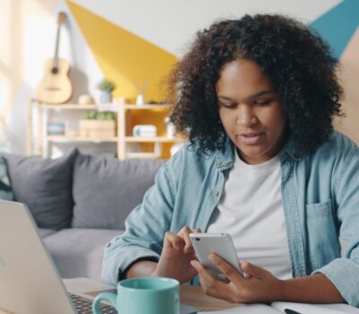 Young woman using phone at desk with laptop.